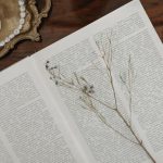 Open vintage book with a dried flower and pearl necklace on a wooden table for a classic look.